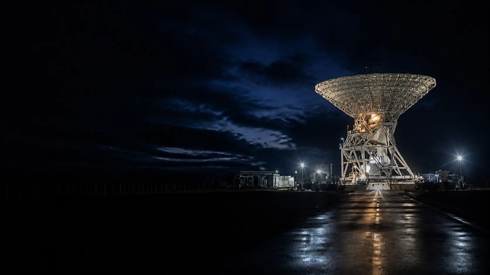 Illuminated satellite communications antenna at a ground station at night